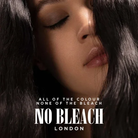 close-up of a young persons face with closed eyes and glossy lips, partially obscured by dark hair, featuring the text ALL OF THE COLOUR NONE OF THE BLEACH NO BLEACH LONDON at the bottom.